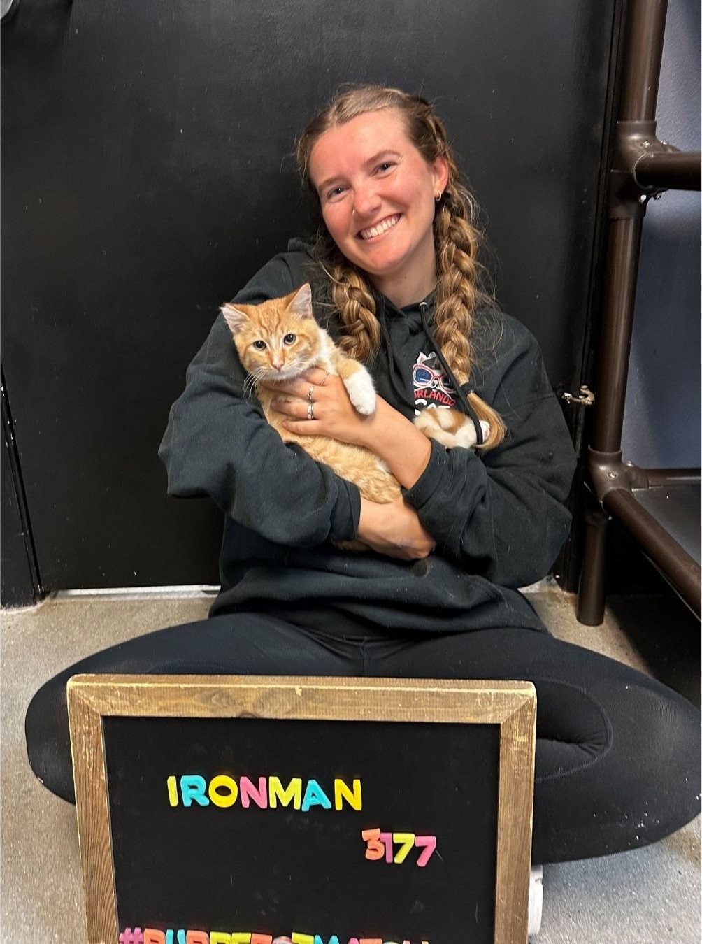 A smiling adopter holding an orange cat named Ironman